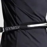 Person schließt eine Bauchtasche, ideal für das handy beim joggen. Der Gurt mit "GYMSH" Schriftzug ist verstellbar.