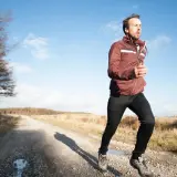 Mann joggt bei 10 Grad auf einem Feldweg. Er trägt eine leichte Jacke und lange Hose, ideal zum **was anziehen joggen 10 grad**.
