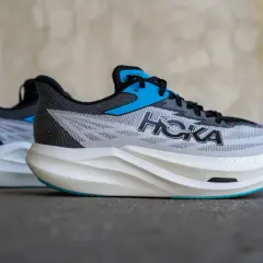 Zwei Hoka Rocket X3 Laufschuhe in Grau mit blauen Akzenten und weißer Sohle stehen nebeneinander.