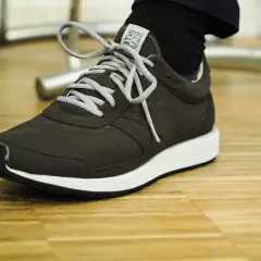 Dunkelgrauer Sneaker mit weißen Schnürsenkeln auf Holzfußboden. Gute Lunge Schuhe Erfahrungen für den Alltag.