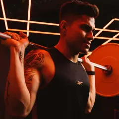 Ein Mann mit Tattoos und einem schwarzen Tanktop hebt eine Hantel. Er schwitzt und konzentriert sich auf sein Dropsatz Training.