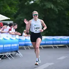 Läuferin mit Startnummer 1424 winkt fröhlich beim Berliner Teamstaffel-Lauf. Zuschauer feuern sie an.