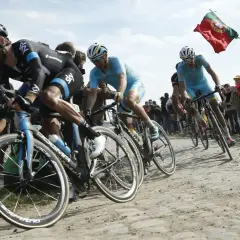 Radprofis kämpfen auf Kopfsteinpflaster, ein portugiesisches Banner weht. Ein Moment, der die Härte und den Ruhm der monumente des radsports einfängt.