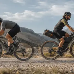 Zwei Radfahrer auf Schotterwegen, die das Abenteuer des Gravelns erleben. Sie fahren mit voll beladenen Rädern durch eine bergige Landschaft.