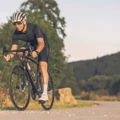 Mann auf Rennrad mit Helm und Brille fährt auf asphaltierter Straße durch hügelige Landschaft. Tolle Rennrad Tipps für deine nächste Tour!