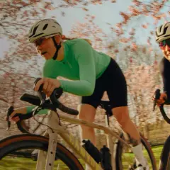Zwei Frauen auf Rennrädern fahren durch eine blühende Kirschbaumallee. Sie sind Teil einer lebendigen Fahrrad-Community, die die Natur genießt.