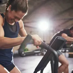 Frau kämpft auf einem Trainingsgerät, während ein Mann im Hintergrund trainiert. Selbst an trainingsfreien Tagen ist Disziplin gefragt.