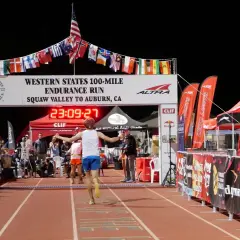 Läufer erreicht das Ziel beim Western States 100-Mile Endurance Run. Die Ziellinie ist mit Flaggen geschmückt, die an einen Ultramarathon in Deutschland erinnern.