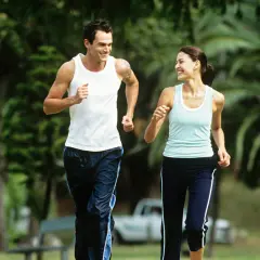 Ein Paar genießt einen Lauf im Park bei angenehmem jogging pace. Sie lachen und schauen sich an, während sie durch das Grün laufen.