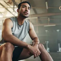 Mann im Fitnessstudio, nachdenklich nach dem Krafttraining. Er fragt sich, ob Cortison eine Rolle spielen könnte.