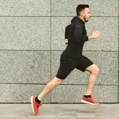 Ein Mann in Schwarz absolviert ein intensives Schwellentraining Laufen vor einer grauen Steinwand.