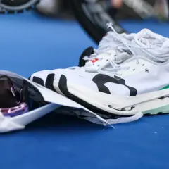 Weiße Laufschuhe mit Carbon-Sohle, bereit für den Wettkampf. Daneben liegen eine Sonnenbrille und ein Energie-Riegel.