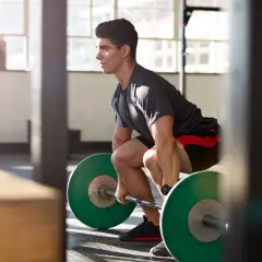 Mann bereitet sich im Fitnessstudio auf das Maximalkraft trainieren vor, greift die Hantel mit grünen Gewichten.