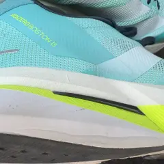 Ein Laufschuh, der adidas adizero boston 13, in Türkis mit gelbem Schriftzug. Die Sohle ist weiß mit einem leuchtend grünen Akzent.