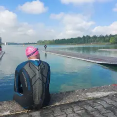 Triathlet in Neoprenanzug und Badekappe sitzt am Beckenrand und wartet auf seinen Start. Die Sonne scheint, die Bedingungen sind perfekt, um zu schwimmen.