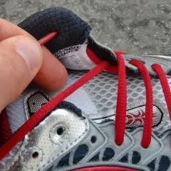 Hand zieht rote Schnürsenkel durch Ösen eines Laufschuhs. So bindet man Laufschuhe richtig für den perfekten Halt.