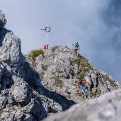 Läufer beim Tschirgant Sky Run auf felsigem Grat, Gipfelkreuz im Hintergrund.