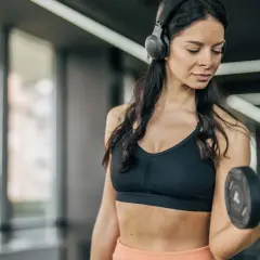 Frau mit Kopfhörern hebt Hantel im Fitnessstudio. Sie fragt sich, wie oft Cardio in der Woche gut ist.
