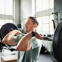 Mann hebt Langhantel im Fitnessstudio. Sein Trainingsplan 2 mal die Woche zahlt sich aus.