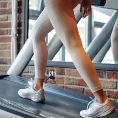 Frau in hellen Leggings und weißen Turnschuhen läuft auf einem Laufband. Sie trainiert für die 12 3 30 Methode.