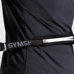 Person schließt eine Bauchtasche, ideal für das handy beim joggen. Der Gurt mit "GYMSH" Schriftzug ist verstellbar.