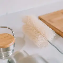 Eine Bürste liegt bereit, um die Trinkflasche zu reinigen. Daneben ein Holzbrett.