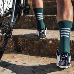 Rennradfahrer tragen lange Socken für Aerodynamik und Schutz. Hier sieht man Beine in grünen Socken mit weißen Streifen, die eine Treppe hochsteigen, neben einem Rennrad.