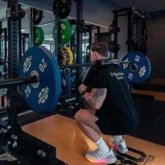 Mann macht Kniebeugen mit Langhantel. Gewichte sind gestapelt. Ein typisches Bild für ein 2er Split Push Pull Training.