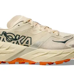 Beiger Hoka Speedgoat 7 Trailrunningschuh mit orangefarbener Vibram-Sohle und dunklem Hoka-Logo.