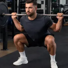 Mann macht Kniebeugen mit Langhantel im Fitnessstudio. Fokus auf Muskelaufbau und Krafttraining.