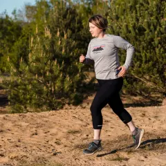 Frau beim **trail running** auf sandigem Untergrund, umgeben von Kiefern und Bäumen.
