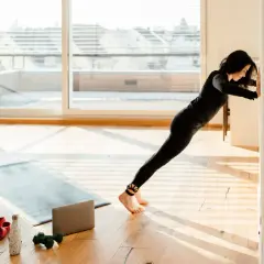 Frau stemmt sich an einer Wand, um Kraft zu bekommen. Trainingsmatte, Hanteln und Wasserflasche liegen bereit.