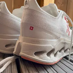 Weiße Laufschuhe, On Cloudsurfer Max, mit markanter Sohle und Schweizer Kreuz-Detail.