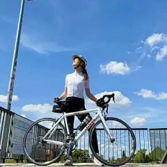Frau mit Rennrad genießt die Sonne nach einem intensiven Intervalltraining Fahrrad. Blauer Himmel mit Wolken.