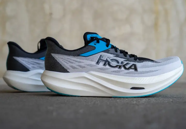 Zwei Hoka Rocket X3 Laufschuhe in Grau mit blauen Akzenten und weißer Sohle stehen nebeneinander.