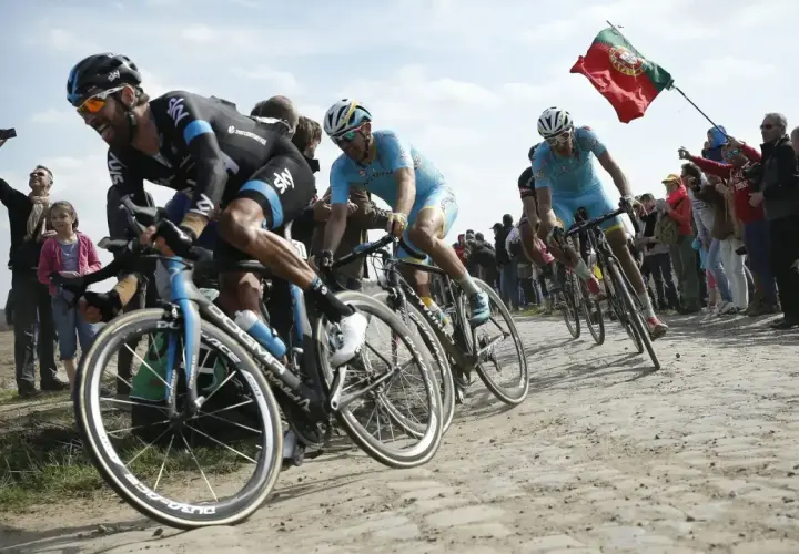 Radprofis kämpfen auf Kopfsteinpflaster, ein portugiesisches Banner weht. Ein Moment, der die Härte und den Ruhm der monumente des radsports einfängt.
