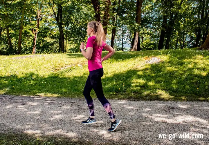 Frau läuft im Wald, um sich aufzulaufen. Sonnenschein und grüne Bäume schaffen eine idyllische Kulisse für ihr Training.