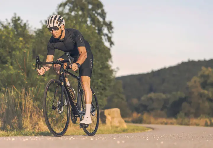 Mann auf Rennrad mit Helm und Brille fährt auf asphaltierter Straße durch hügelige Landschaft. Tolle Rennrad Tipps für deine nächste Tour!