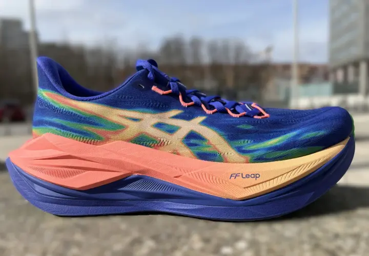 Blauer Laufschuh mit Regenbogenmuster und orangefarbener Sohle, bereit für einen superblast 3.