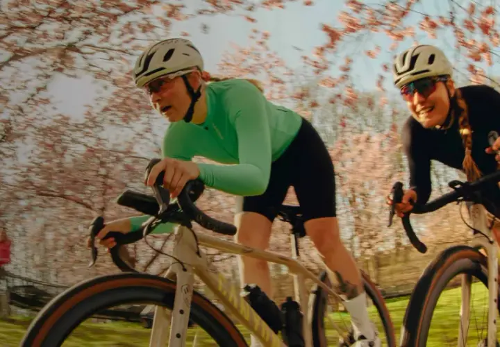 Zwei Frauen auf Rennrädern fahren durch eine blühende Kirschbaumallee. Sie sind Teil einer lebendigen Fahrrad-Community, die die Natur genießt.
