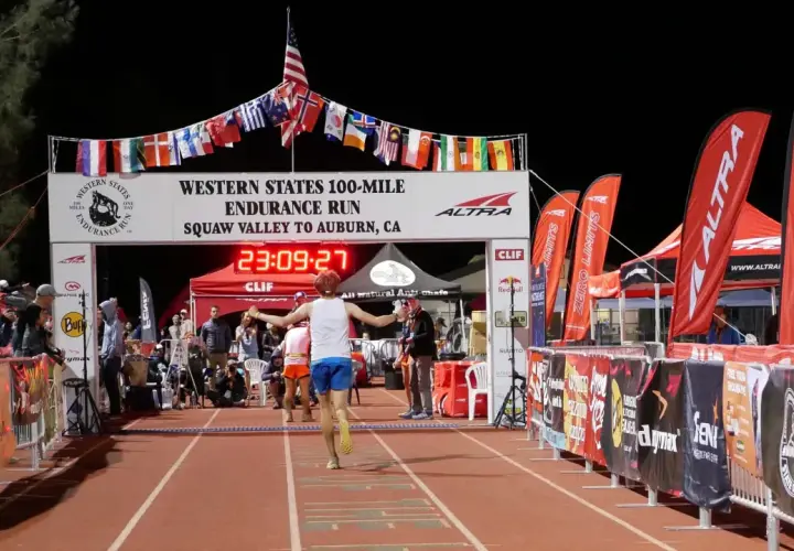 Läufer erreicht das Ziel beim Western States 100-Mile Endurance Run. Die Ziellinie ist mit Flaggen geschmückt, die an einen Ultramarathon in Deutschland erinnern.