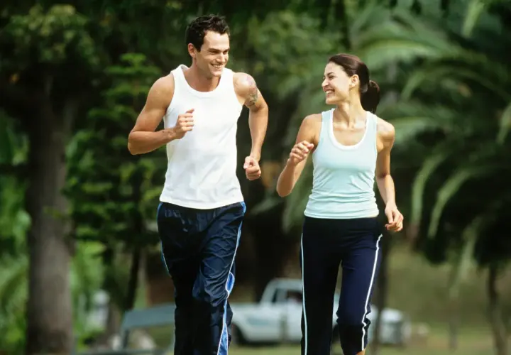Ein Paar genießt einen Lauf im Park bei angenehmem jogging pace. Sie lachen und schauen sich an, während sie durch das Grün laufen.