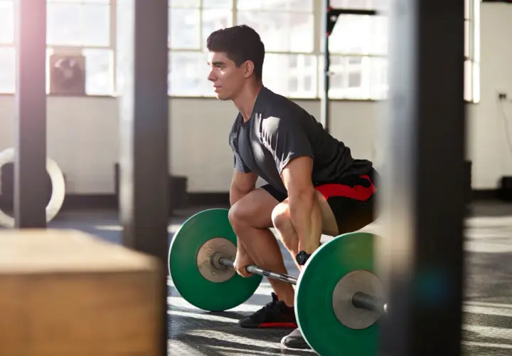 Mann bereitet sich im Fitnessstudio auf das Maximalkraft trainieren vor, greift die Hantel mit grünen Gewichten.