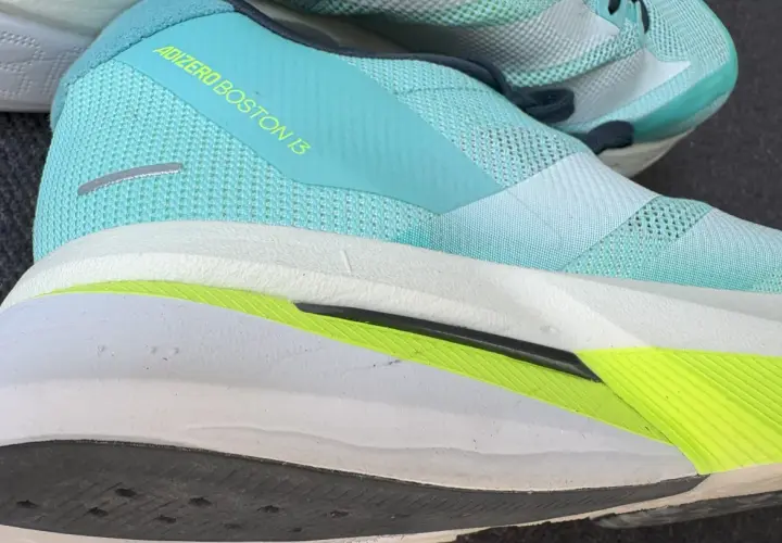 Ein Laufschuh, der adidas adizero boston 13, in Türkis mit gelbem Schriftzug. Die Sohle ist weiß mit einem leuchtend grünen Akzent.