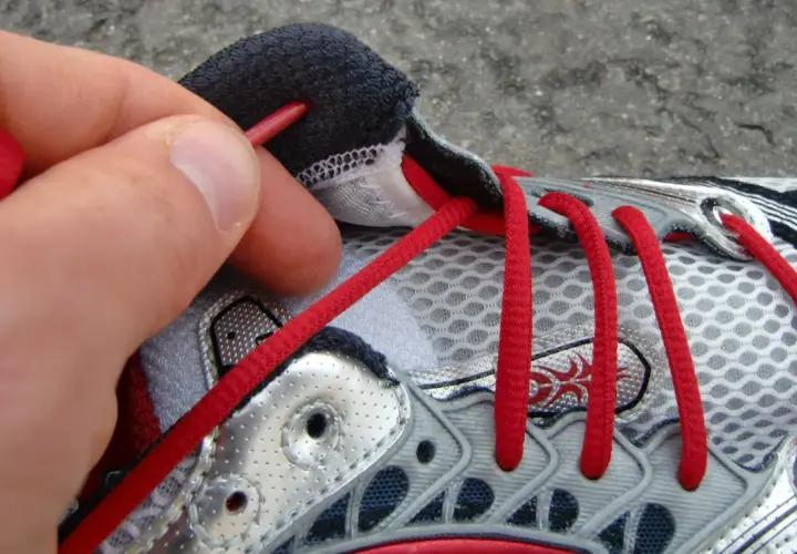 Hand zieht rote Schnürsenkel durch Ösen eines Laufschuhs. So bindet man Laufschuhe richtig für den perfekten Halt.