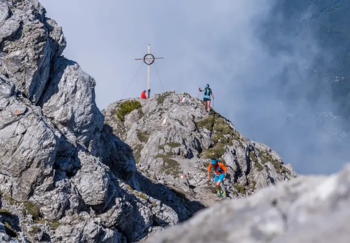 Läufer beim Tschirgant Sky Run auf felsigem Grat, Gipfelkreuz im Hintergrund.