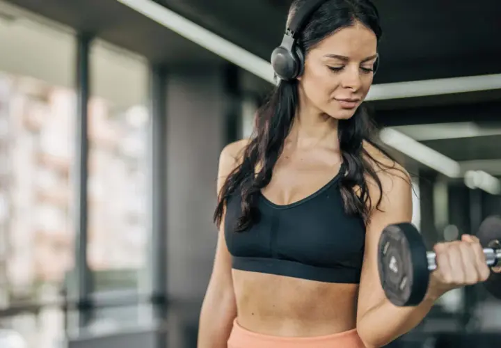 Frau mit Kopfhörern hebt Hantel im Fitnessstudio. Sie fragt sich, wie oft Cardio in der Woche gut ist.