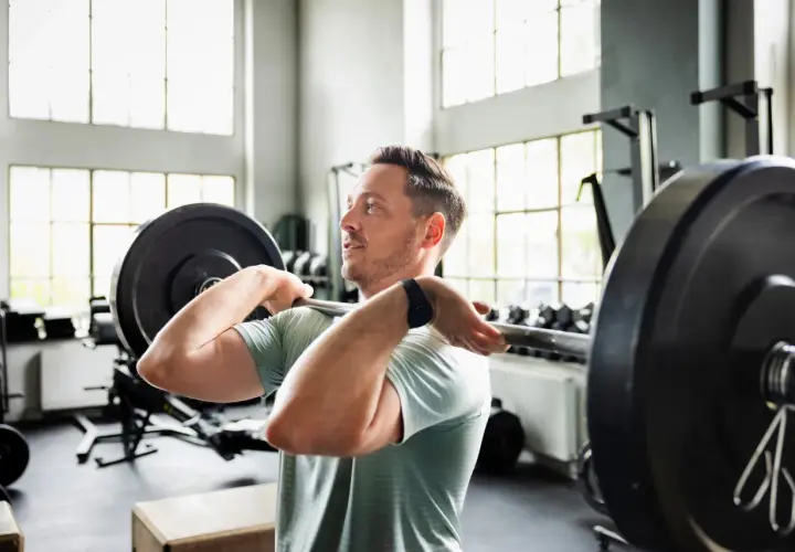Mann hebt Langhantel im Fitnessstudio. Sein Trainingsplan 2 mal die Woche zahlt sich aus.