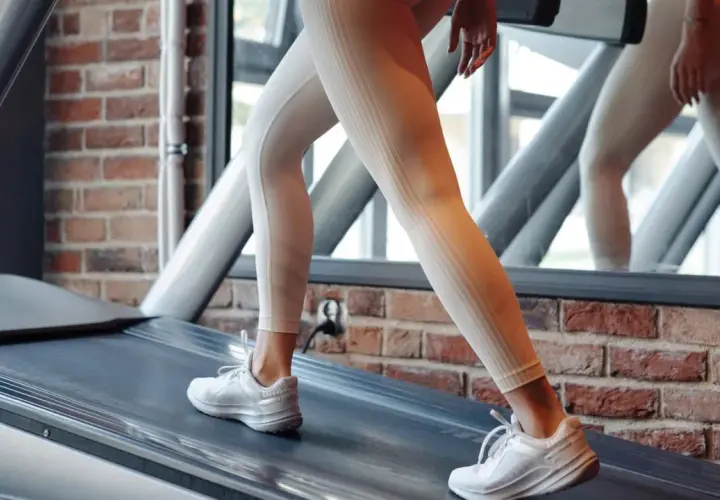 Frau in hellen Leggings und weißen Turnschuhen läuft auf einem Laufband. Sie trainiert für die 12 3 30 Methode.