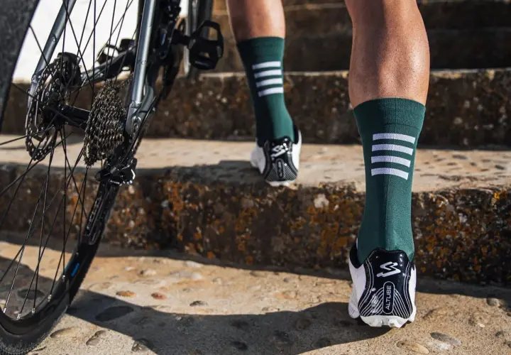 Rennradfahrer tragen lange Socken für Aerodynamik und Schutz. Hier sieht man Beine in grünen Socken mit weißen Streifen, die eine Treppe hochsteigen, neben einem Rennrad.